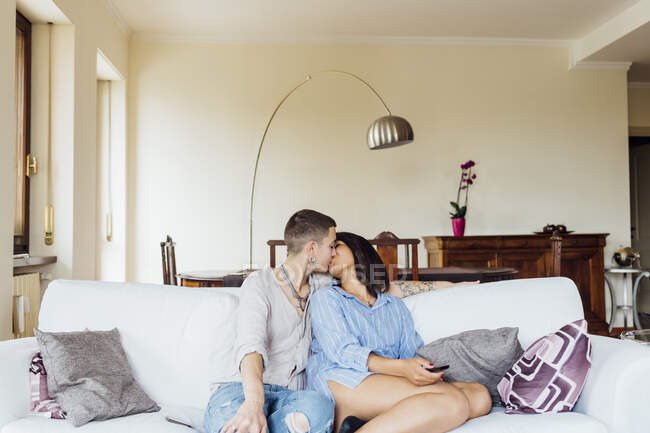 Namoradas afetuosas beijando enquanto sentado no sofá na sala de estar — Fotografia de Stock
