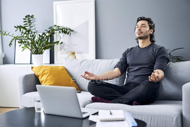 Мужчина медитирует, сидя дома на диване — стоковое фото