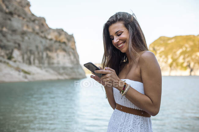 Smiling woman using smart phone at Pantano de Santa Ana, Castillonroy, Spain — Stock Photo