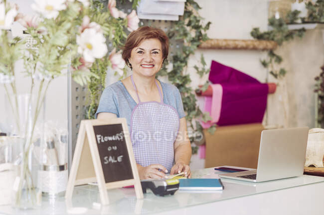 Sorridente fiorista donna matura in piedi alla cassa in negozio di fiori — Foto stock
