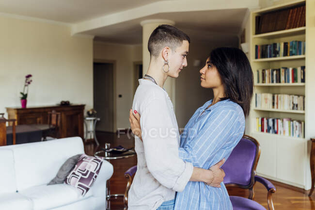 Молодые женщины смотрят друг на друга, обнимаясь в гостиной — стоковое фото