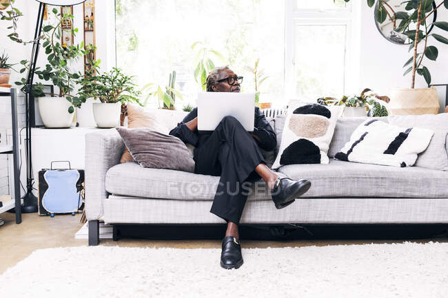 Male professional looking away while sitting with laptop on sofa at home — Stock Photo