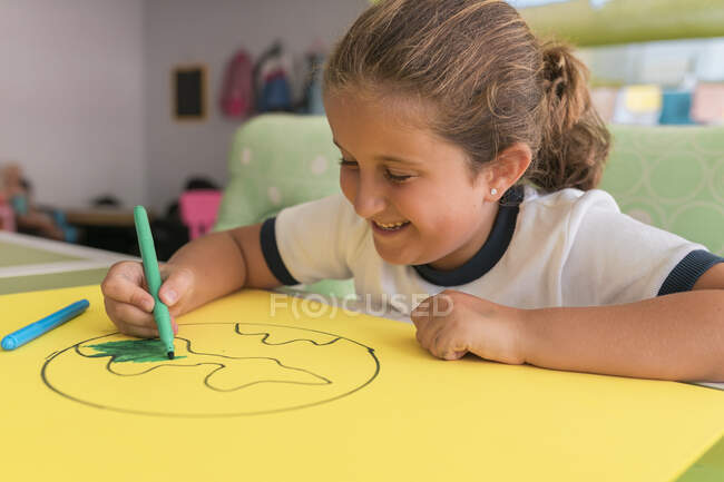 Smiling cute girl coloring earth sketch at home — Stock Photo