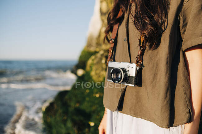 Giovane donna con macchina fotografica in piedi sulla spiaggia — Foto stock