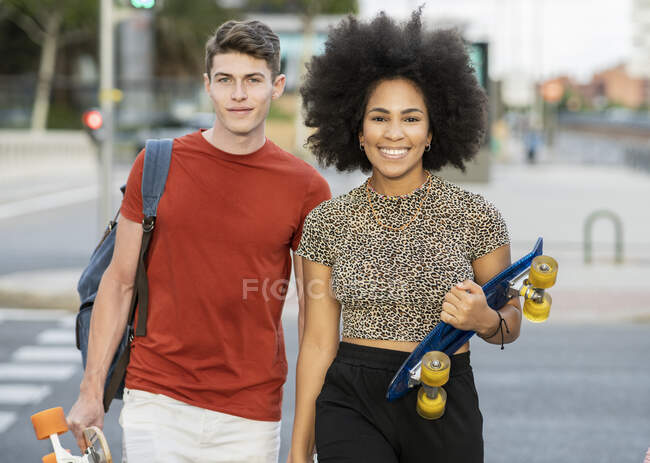 Pareja joven caminando mientras sostiene patinetas - foto de stock