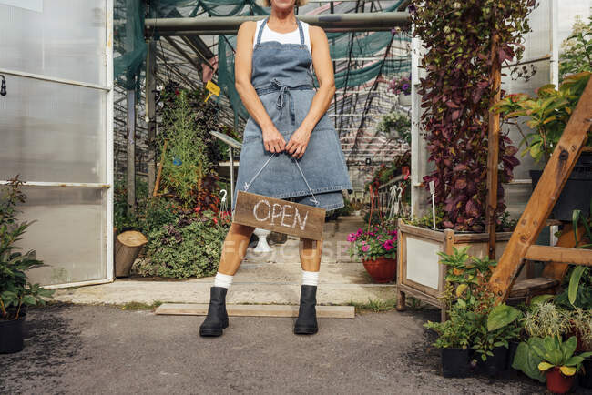 Serra femminile che tiene il segno aperto di legno alla porta della serra — Foto stock