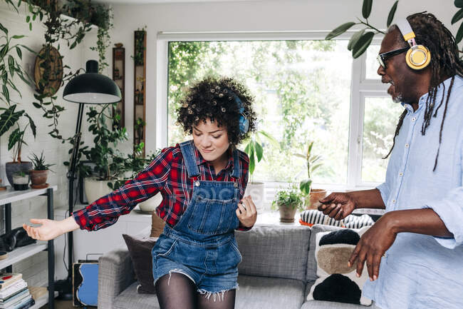 Mujer escuchando música a través de auriculares mientras baila con el hombre en la sala de estar - foto de stock