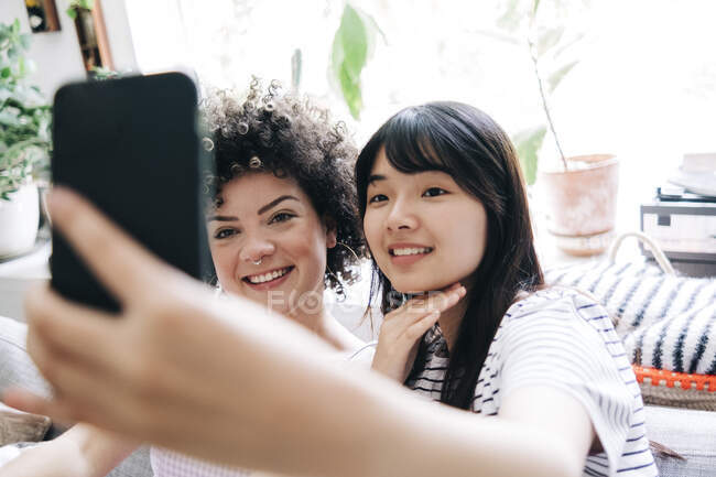 Усміхаючись, жінки - друзі роблять самовідтворення через мобільний телефон удома. — стокове фото