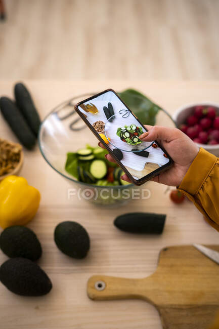 Woman taking photo of vegetables through smart phone at table — Stock Photo
