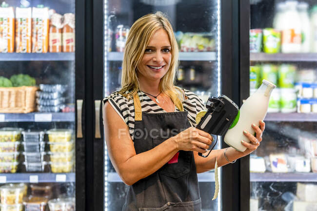 Vendedora madura etiquetando botella de leche en la tienda - foto de stock