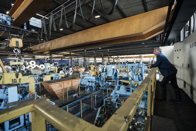 Homme d'affaires regardant les machines de fabrication tout en s'appuyant sur la rampe — Photo de stock