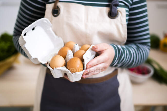 Mulher com avental segurando caixa de ovos em casa — Fotografia de Stock