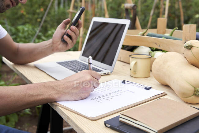Mid adult male farmer writing on clipboard while sitting at table — Stock Photo
