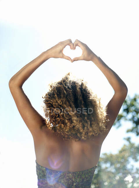 Жінка з кучерявим волоссям формує серце руками в сонячний день. — стокове фото