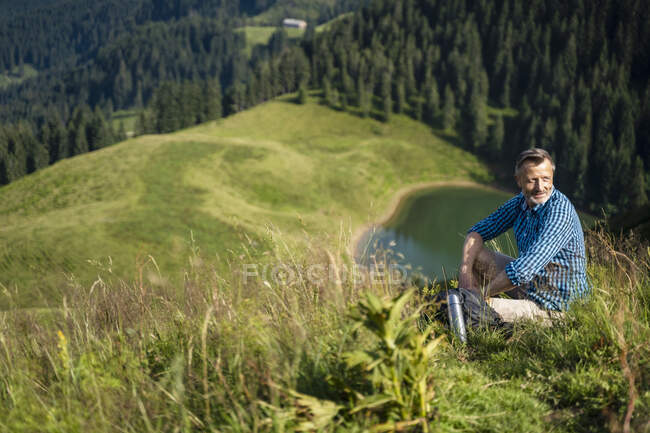 Smiling male hiker resting while sitting on mountain — Stock Photo