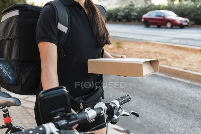 Female essential worker holding courier package while wheeling cycle — Stock Photo
