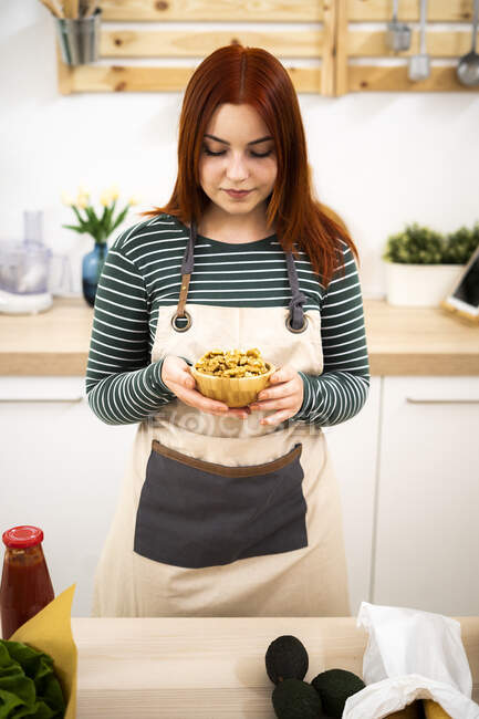 Женщина держит чашу с грецким орехом, стоя на кухне — стоковое фото