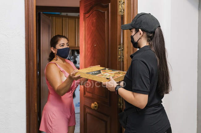 Женщина важный работник доставки пиццы коробку для зрелых клиентов в дверях — стоковое фото