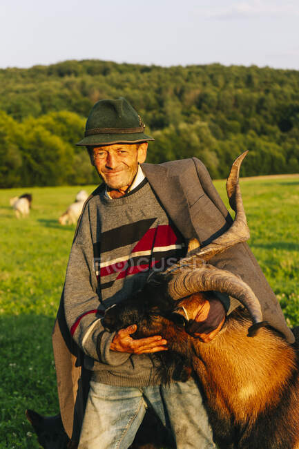Sonriente pastor macho mayor abrazando cabra - foto de stock