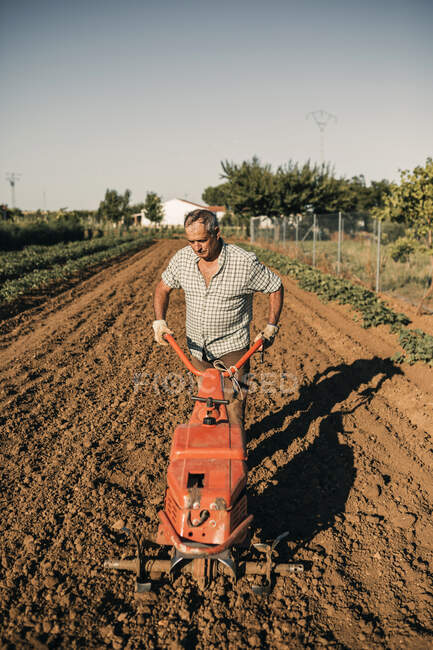Trabalhador agrícola masculino arar terra através de grade durante o dia ensolarado — Fotografia de Stock