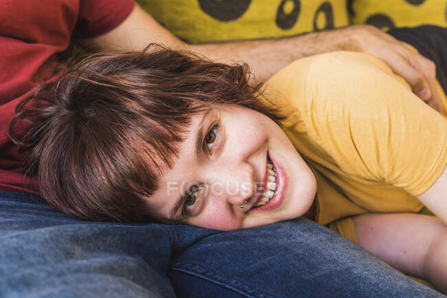 Mujer adulta sonriendo mientras está acostada en el regazo del novio en la sala de estar - foto de stock
