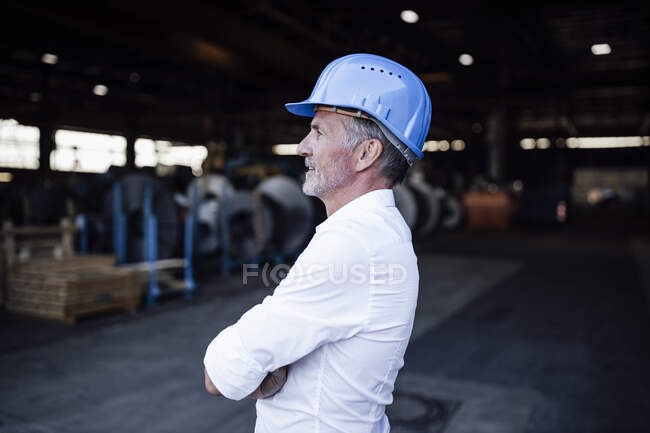Ingeniero masculino con casco de pie con los brazos cruzados en la industria del metal - foto de stock
