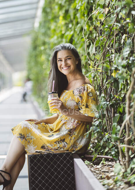 Souriant belle femme mature assise avec pot devant les plantes — Photo de stock
