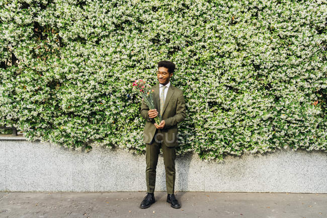 Uomo d'affari sorridente guardando il fiore mentre in piedi di fronte alle piante sul sentiero — Foto stock