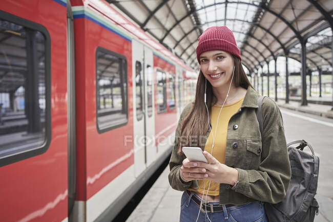 Bela passageira feminina com telefone celular sorrindo em pé de trem na estação ferroviária — Fotografia de Stock