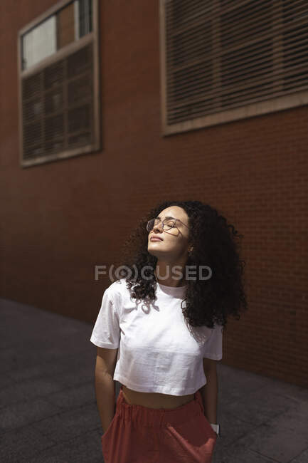 Giovane donna con le mani in tasca di fronte all'edificio durante la giornata di sole — Foto stock