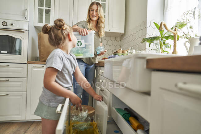 Madre guardando figlia gettare spazzatura nel cestino del riciclaggio in cucina — Foto stock