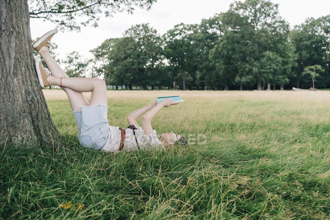 Mujer leyendo libro mientras se relaja en la hierba en el parque - foto de stock