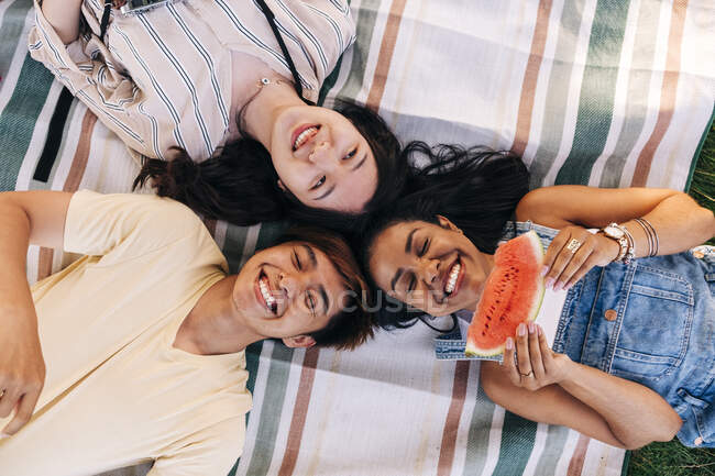 Amigos felizes deitados juntos no cobertor de piquenique — Fotografia de Stock