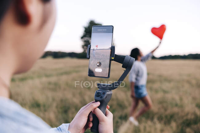 Жінка знімає друга з повітряною кулькою через смартфон у парку. — стокове фото