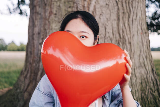 Женщина покрывает лицо красным шаром в форме сердца в парке — стоковое фото