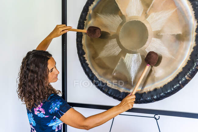 Female sound therapist playing gong with mallets in studio — Stock Photo