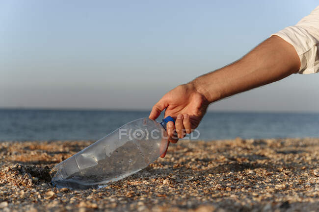 Человек собирает пластиковые бутылки на песке на пляже — стоковое фото