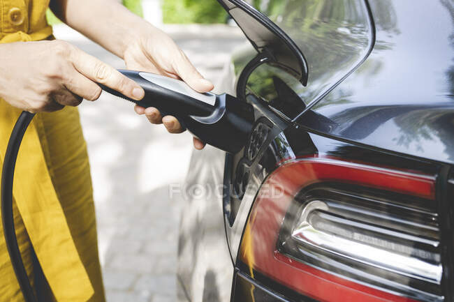 Mulher madura segurando cabo por plugue de carro elétrico — Fotografia de Stock