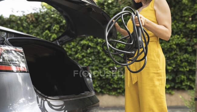 Woman holding cable while standing by open car trunk — Stock Photo