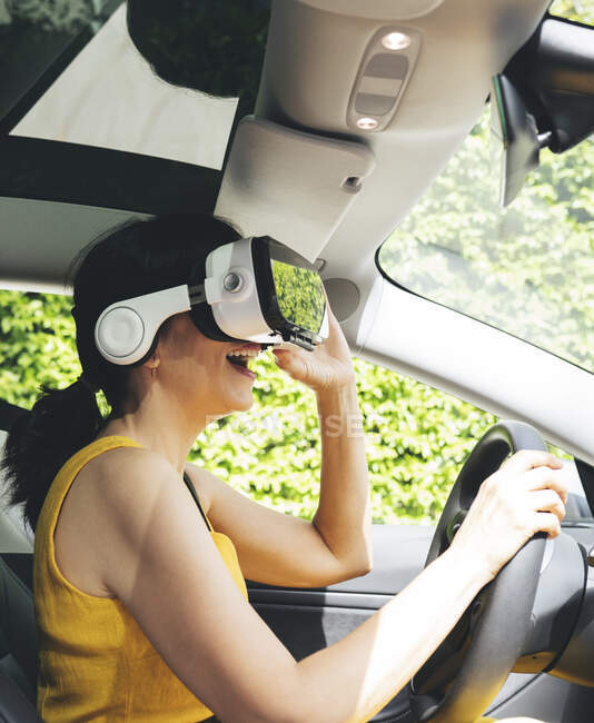 Mulher vestindo simulador de realidade virtual enquanto dirige carro elétrico — Fotografia de Stock