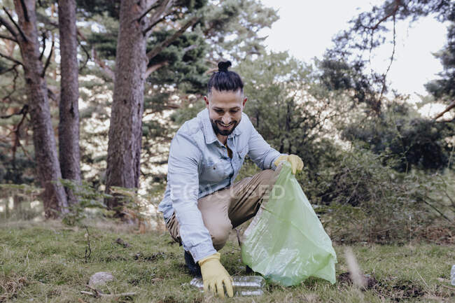 Hombre voluntario recogiendo botella de plástico mientras se agacha en el bosque - foto de stock
