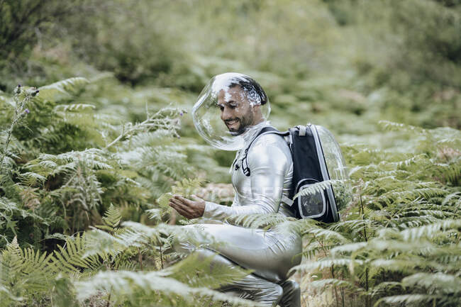 Ambientalista masculino sorridente com terno protetor examinando plantas na floresta — Fotografia de Stock