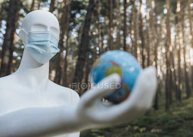 Робот в защитной маске держит земной шар в лесу — стоковое фото