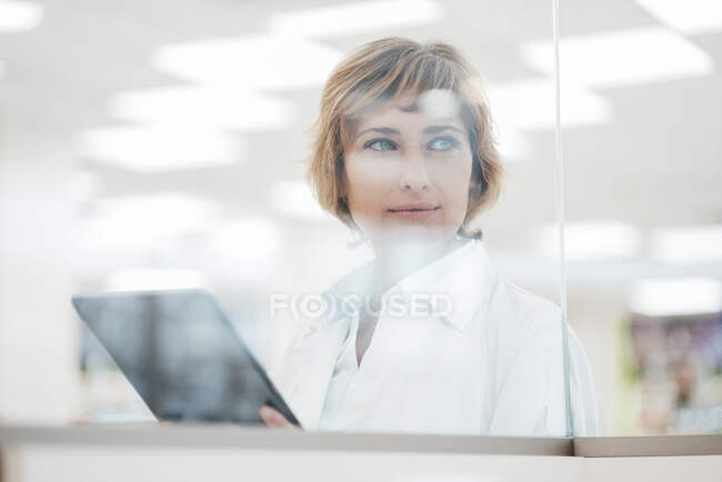 Chimica femminile con tablet digitale che guarda attraverso la finestra di vetro — Foto stock