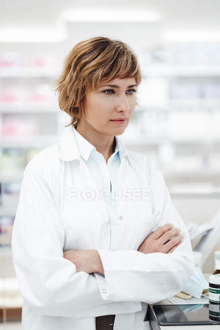 Farmacêutica feminina de pé com os braços cruzados na farmácia — Fotografia de Stock