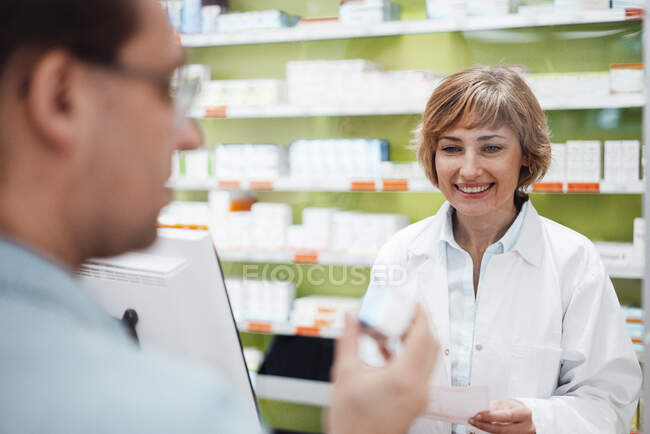 Sorridente farmacista femminile che guarda la medicina di controllo del cliente — Foto stock