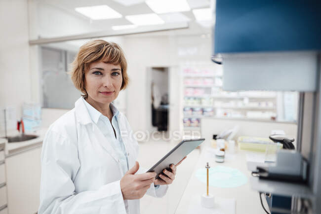 Profesional femenino sosteniendo tableta digital mientras está de pie en el laboratorio - foto de stock