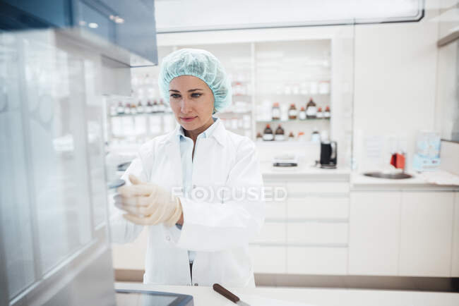 Profesional femenino que usa gorra quirúrgica investigando mientras trabaja en laboratorio - foto de stock