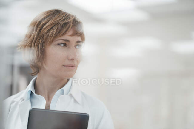 Experiencia femenina madura con tableta digital mirando hacia otro lado en la farmacia - foto de stock