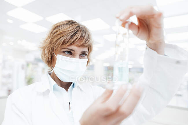 Farmacéutica usando mascarilla protectora analizando en laboratorio - foto de stock
